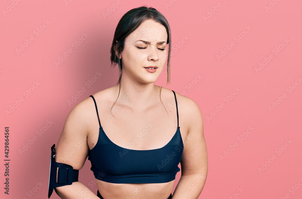 Young hispanic woman wearing sportswear with hand on stomach because nausea, painful disease feeling unwell. ache concept.