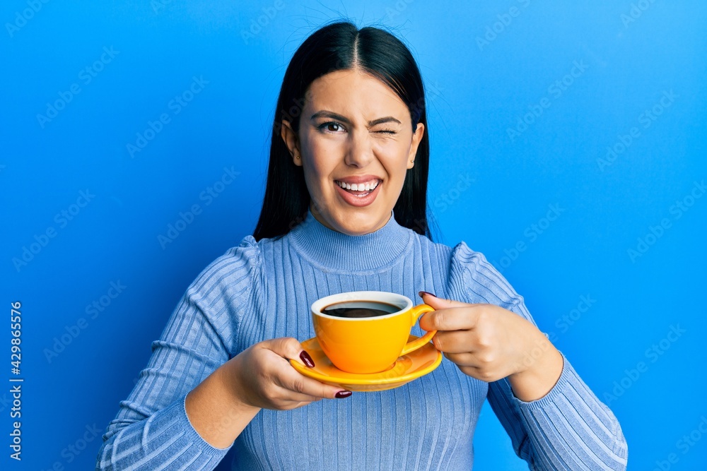 Beautiful brunette woman drinking a yellow cup of black coffee winking looking at the camera with sexy expression, cheerful and happy face. Beautiful brunette woman drinking a yellow cup of black coffee winking looking at the camera with sexy expression, cheerful and happy face.