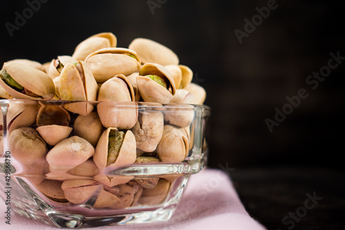 Some pistachios in a glass bowl on a black wooden table 