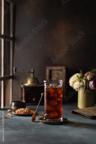Glass of iced coffee on the table near the wooden window with vintage coffeegrinder on background.Cold drink.