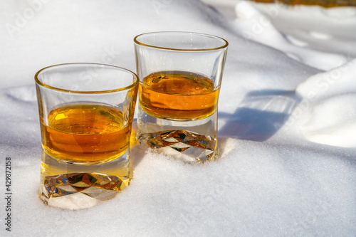 Glasses of cold scotch single malt whisky on white snow