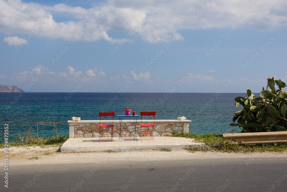 Obraz premium two empty red chairs and a table by the sea on Crete island (Greece)