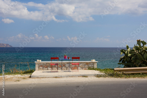 two empty red chairs and a table by the sea on Crete island (Greece)