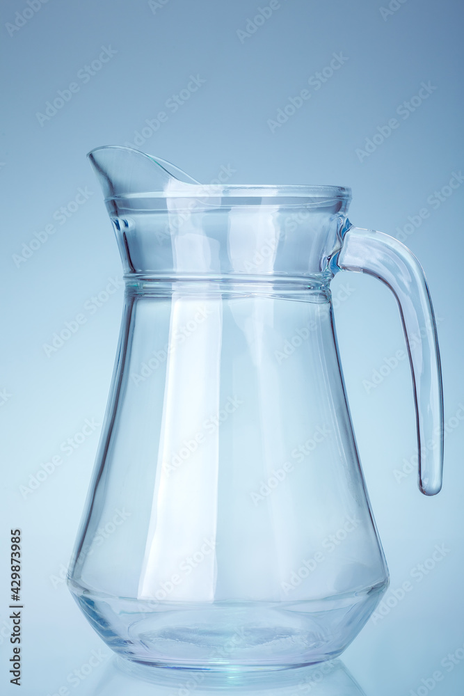 glass transparent water jug with handle and spout isolated on light cold background kitchen utensils. glass transparent water jug with handle and spout isolated on light cold background kitchen utensils.