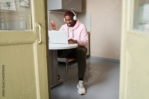 Multiracial employee in headphones using laptop and looking at the screen