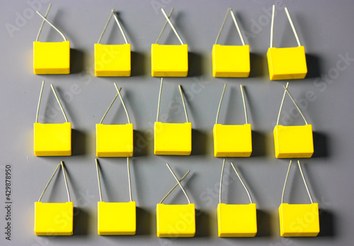 Yellow film capacitors isolated on gray background top view. Many square shape plastic electronic radio components on the gray surface with contrast shadows flatly. Selective focus.