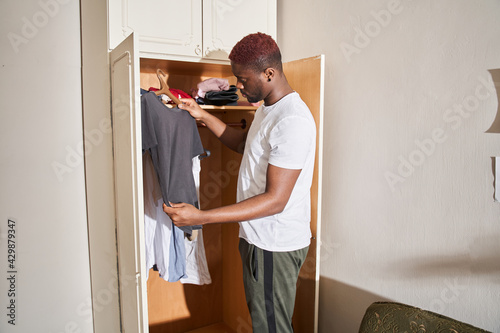 Man holding his t shirt and examines his clothes while standing near the closet