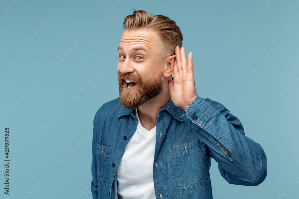 Bearded hipster blonde man with hand over ear listening an hearing to rumor or gossip over blue background. Bearded hipster blonde man with hand over ear listening an hearing to rumor or gossip over blue background.