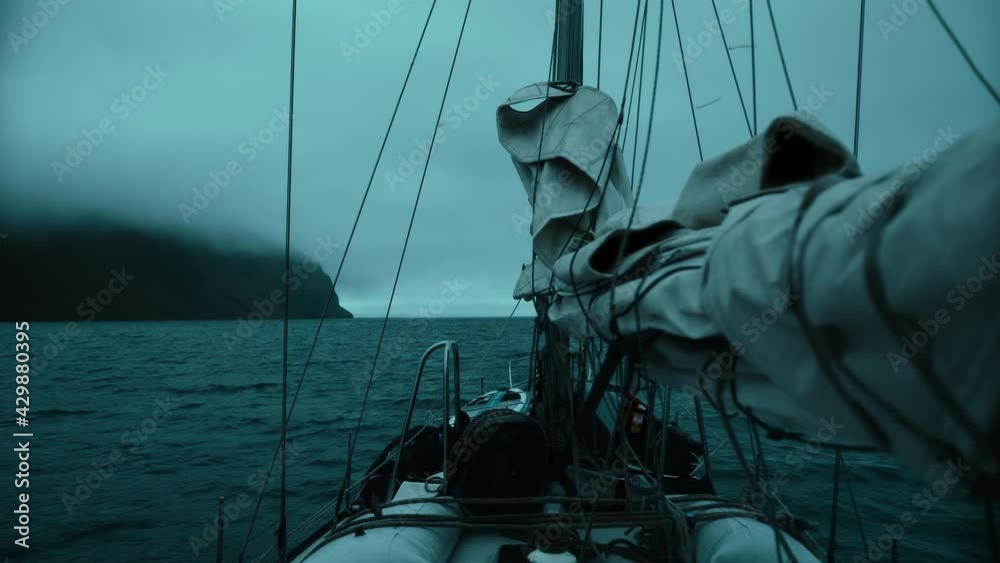 Yacht with lowered sails sails on the night ocean among the fog, swaying on the waves. 