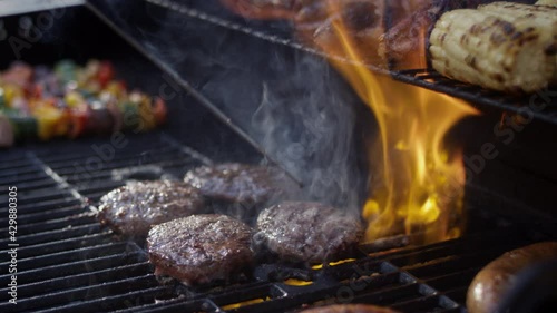 Huge flames shoot up around delicious charred burgers at a bbq