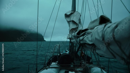 Yacht with lowered sails sails on the night ocean among the fog, swaying on the waves. 
