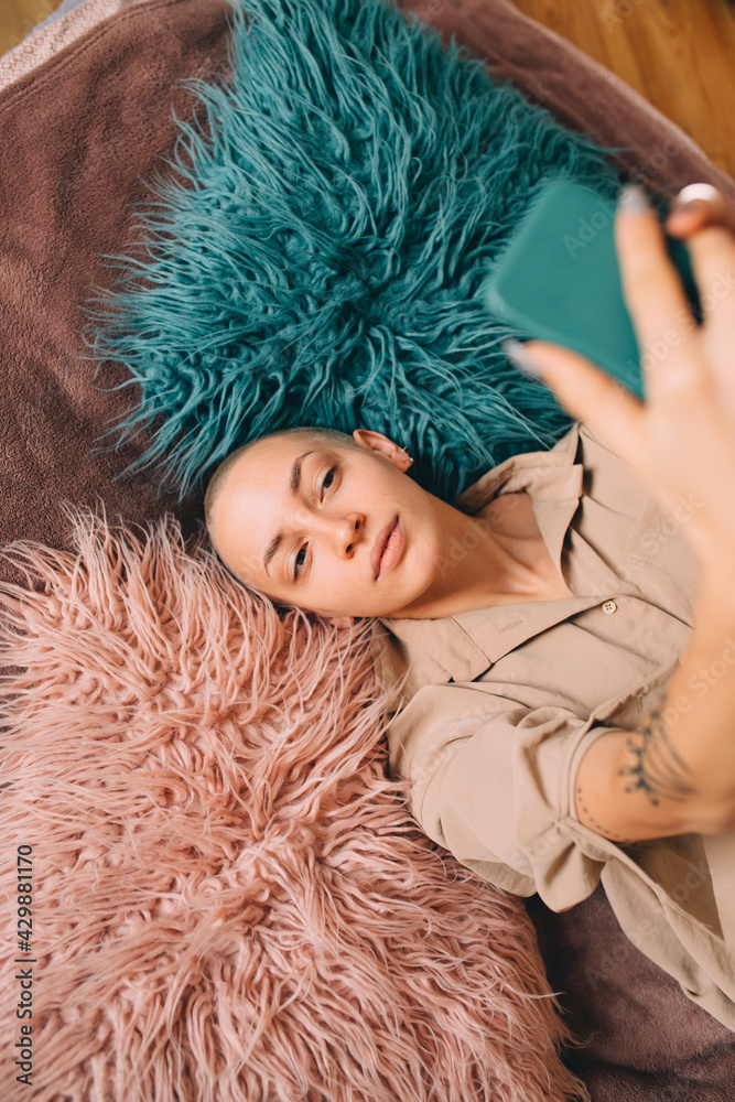 Girl with short haircut laying at the fur and making selfie at her smartphone Girl with short haircut laying at the fur and making selfie at her smartphone