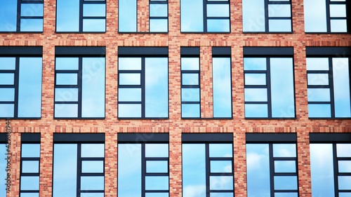 Modern brick and glass facade of the office building. A contrasting combination of sky and brick texture on a building. Architectural facade of a red brick building..