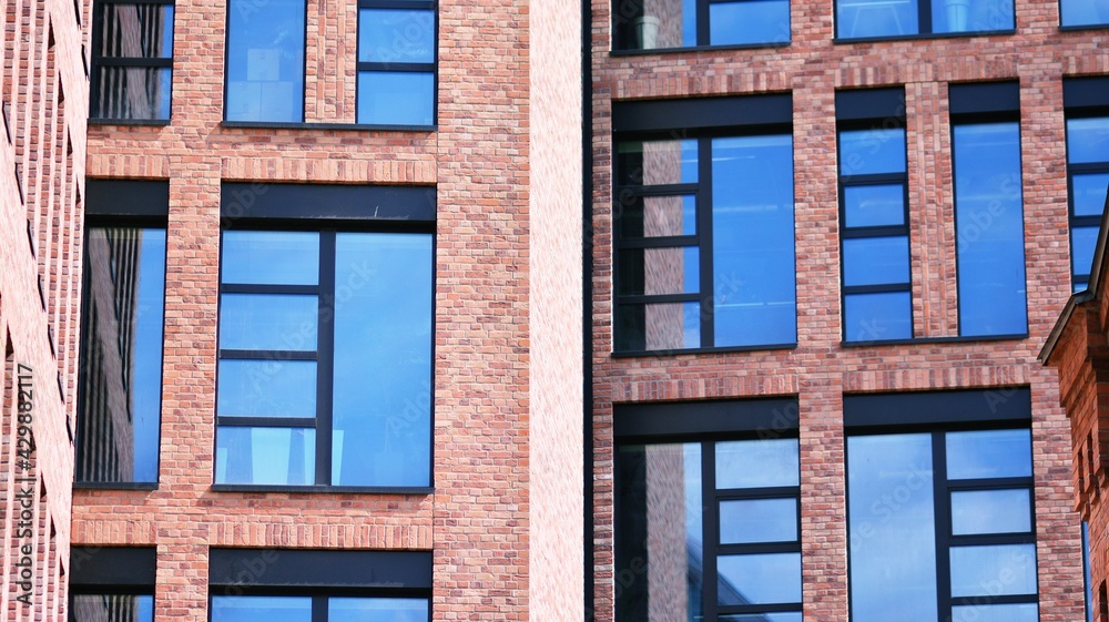 Fototapeta premium Modern brick and glass facade of the office building. A contrasting combination of sky and brick texture on a building. Architectural facade of a red brick building..