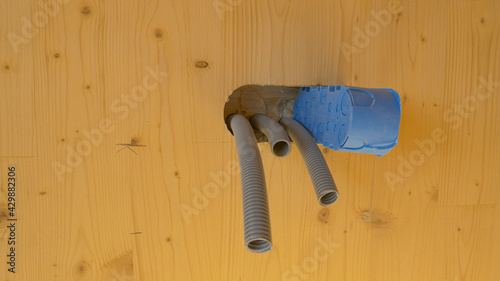 CLOSE UP: Corrugated conduits and blue socket box protrude out of wooden wall.