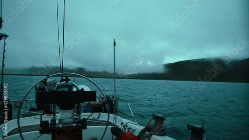 Yacht with lowered sails sails on the night ocean among the fog, swaying on the waves. 