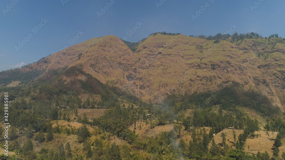 mountains with farmlands, village, fields with crops, trees. Aerial view mountain landscape slopes mountains covered with green forest. Java, Indonesia.
