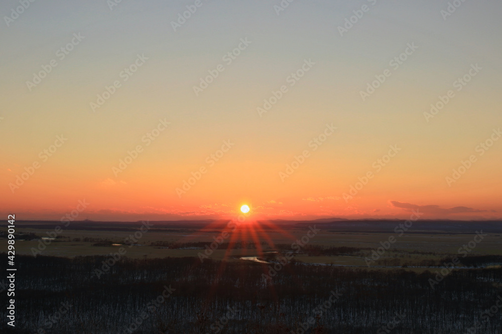 釧路湿原に沈む夕日と夕日に照れされて輝く釧路川