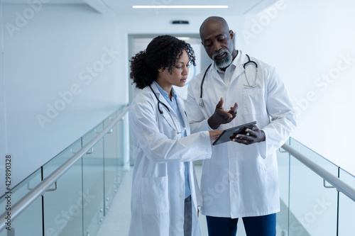 Diverse male and female doctor talking seriously and looking at digital tablet in hospital corridor