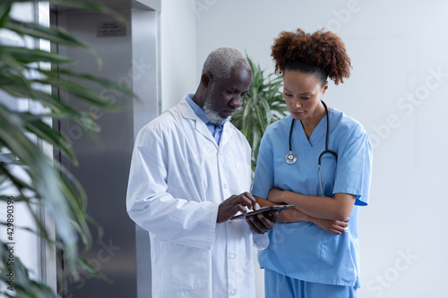 Diverse male and female doctors using tablet and discussing in hospital corridor