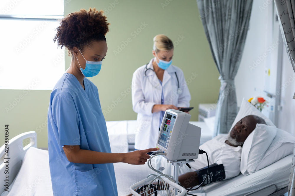 Mixed race female doctor wearing face mask using blood pressure monitor in patient room Mixed race female doctor wearing face mask using blood pressure monitor in patient room