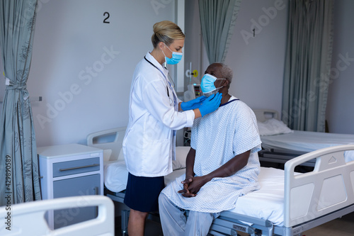 Caucasian female doctor wearing face mask palpating lymph nodes of african american male patient