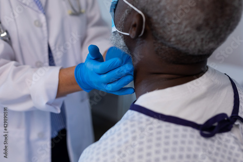 Caucasian female doctor palpating lymph nodes of african american male patient wearing mask photo