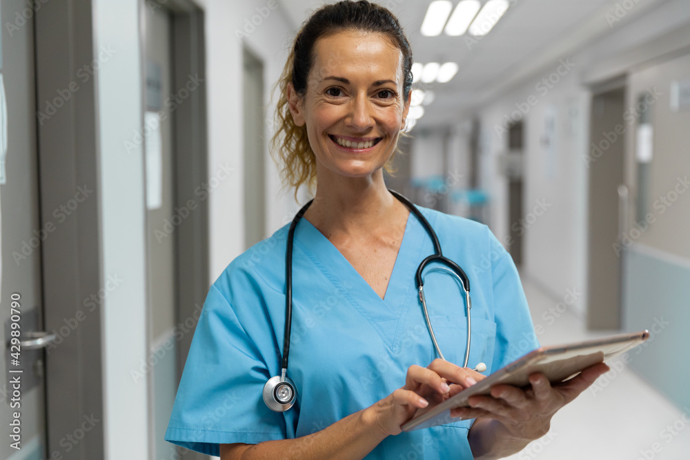 Portrait of mixed race female doctor stading on corridor smiling using laptop Portrait of mixed race female doctor stading on corridor smiling using laptop