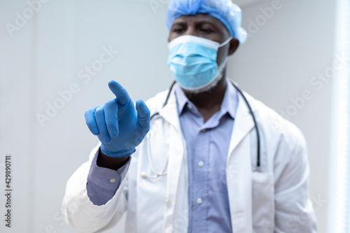 African american male doctor wearing face mask using virtual interactive interface