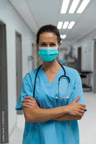 Portrait of mixed race female doctor wearing face mask standing in hospital corridor