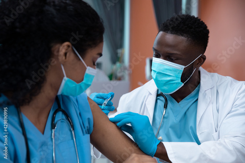 Mixed race couple of doctors wearing face masks making injection