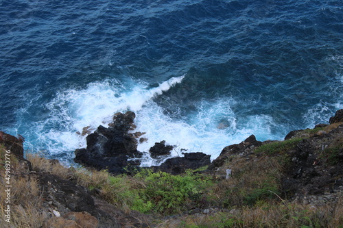 Fototapeta Naklejka Na Ścianę i Meble -  Looking down a cliff to see waves crashing against the rocks below on Oahu, Hawaii.