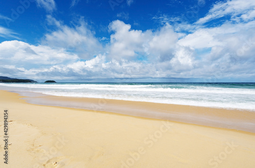 Beautiful sandy beach with wave seafoam clashing on sandy shore turquoise ocean water and blue sky white clouds over sea Natural background for summer vacation Travel website