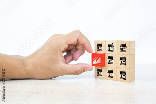 Franchise, Hand choose graph icon on cube wooden toy blocks stacked with franchise business store icon for growth and financial marketing planning and bank loan for branch expansion franchisee.