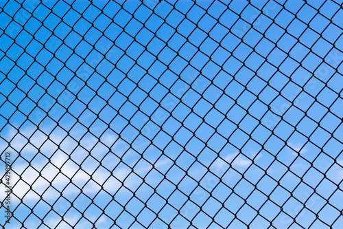 Abstract image showing a latticework of a chain fence covering the entire blue sky. Versatile for concepts like lack of freedom, humanitarian causes, captivity, slavery, limitations, restrictions