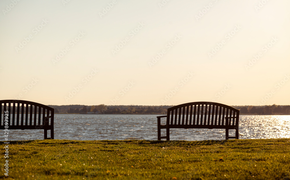 Wooden isolated benches on the waterfront overlooking a calm river at sunset. Abstract versatile image with copy space. Relaxing, leisure, tranquil concepts.