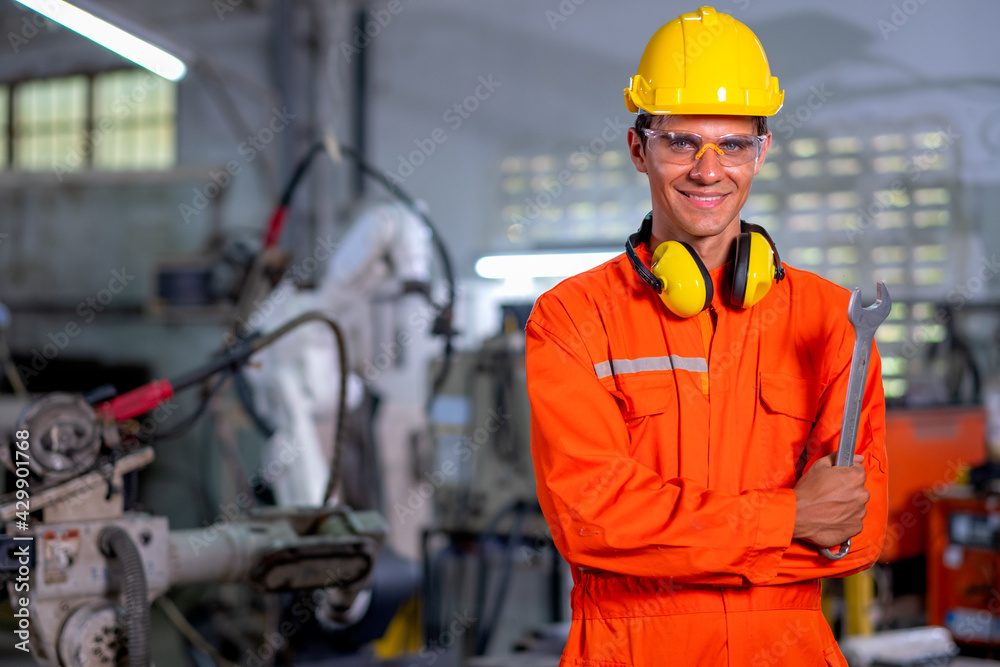 Portrait of factory worker man with protection suit stand with confidence smiling in front of industrial robotic machine in workplace area. Employee support system help in industrial business concept. Portrait of factory worker man with protection suit stand with confidence smiling in front of industrial robotic machine in workplace area. Employee support system help in industrial business concept.