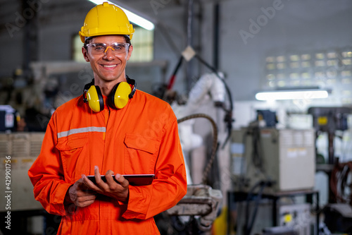 Portrait of factory worker man with protection suit stand with confidence smiling in front of industrial robotic machine in workplace area. Employee support system help in industrial business concept.