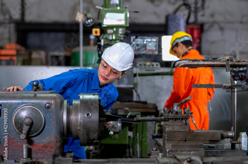 Asian factory worker woman look to part of the machine and inspect the function while her co-worker work with other machine in the background. Maintenance and check system support industrial business.