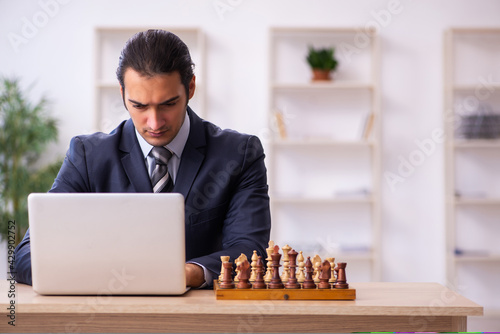 Young male employee playing chess at workplace