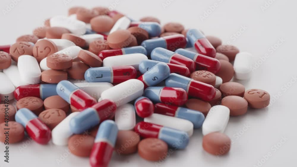A pile of mixed prescription pills rotates on a white surface