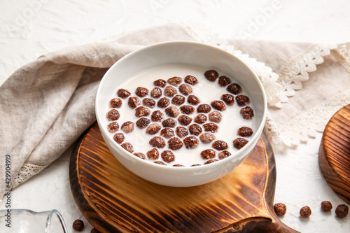 Bowl with chocolate corn balls and milk on light background