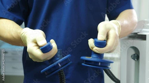 Resuscitator holding defibrillation electrode in hand. Preparing for defibrillation to save life. Equipment in modern clinic. Doctor getting ready to give resuscitation to patient in emergency room. 4