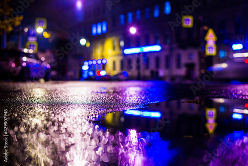 Autumn rainy night in the city. Empty street. Parked cars. Residential buildings in the city center. Colorful colors. Close up view from the level of the puddle on the pavement.
