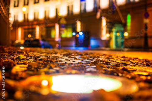 Rainy autumn evening in the city. Fallen leaves. Stone paved sidewalk. Light from the windows of houses. Spotlight on the sidewalk. Colorful colors. Close up view from the pavement level.