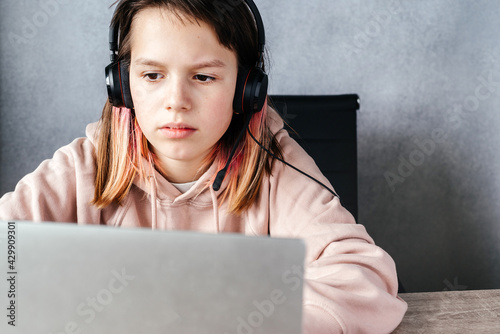 A girl wearing headphones and using her laptop while studying online, e-learning and online education concept