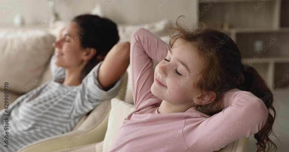Calm little daughter relax with mom leaned on cozy sofa, close up focus on kid. Peaceful family closing eyes put hands behind head enjoy fresh conditioned air inside of modern flat. No stress concept Calm little daughter relax with mom leaned on cozy sofa, close up focus on kid. Peaceful family closing eyes put hands behind head enjoy fresh conditioned air inside of modern flat. No stress concept