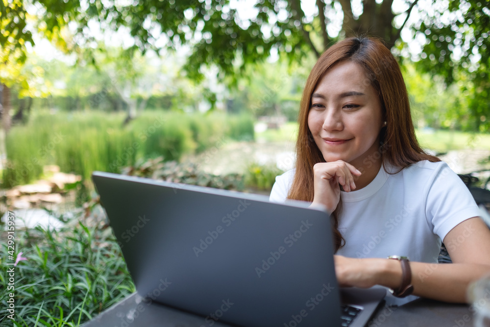 A young asian woman working and typing on laptop keyboard while sitting in the park A young asian woman working and typing on laptop keyboard while sitting in the park