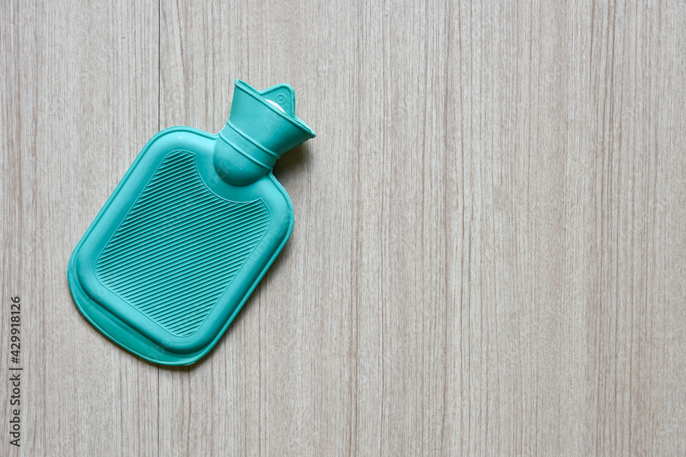 green hot water bottle bag made of rubber on wooden table, with copy space ready for adding text green hot water bottle bag made of rubber on wooden table, with copy space ready for adding text