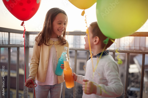 Sticker Little girl and boy holding balloons and spending a wonderful time together on the terrace of an apartment